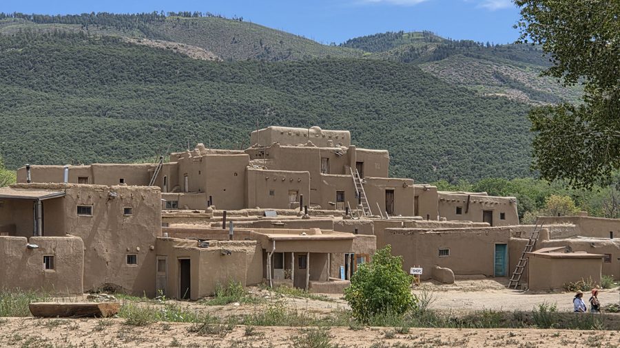 Adobe structures at Taos Pueblo below a forested mountain